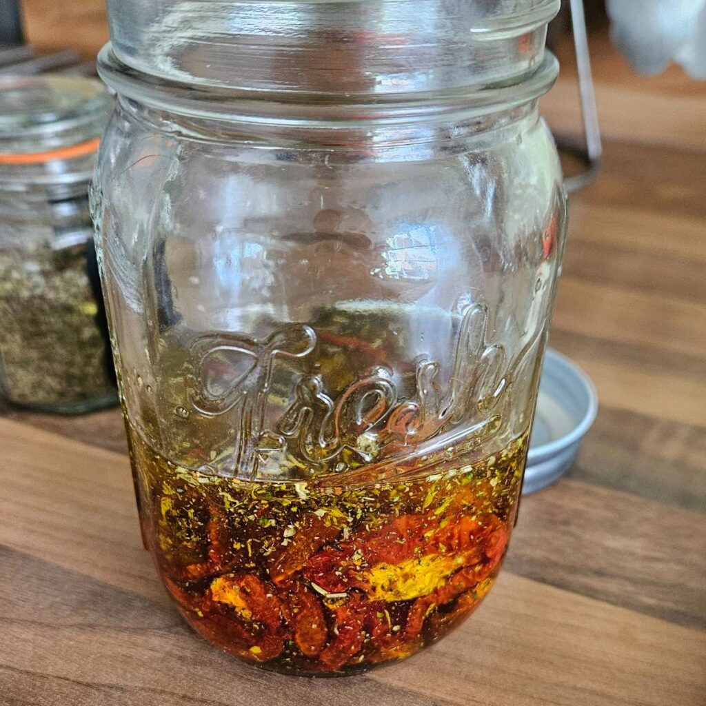 Homemade sun dried tomatoes in olive oil in a glass jar on the kitchen side.