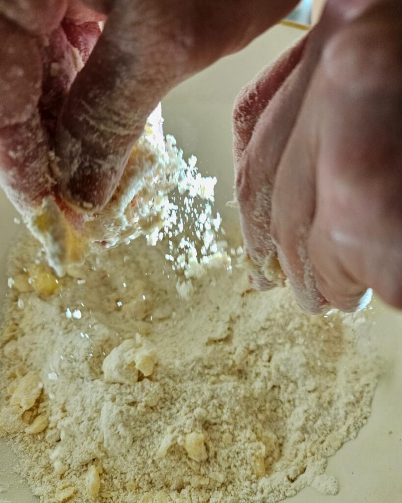 Rubbing in butter to a flour mixture to make the dough for homemade cherry scones.